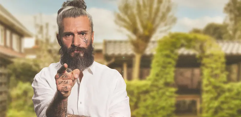 EIn Mann steht mit erhobenem Zeigefinger im Garten